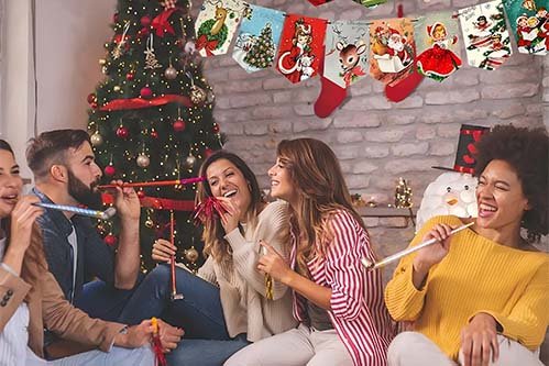 A group of people are enjoying a Christmas party, with a decorated Christmas tree, festive banners, and party blowers, all having a great time.