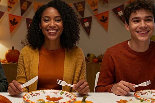 Two people are smiling at a Thanksgiving dinner, with "Happy Thanksgiving" plates.